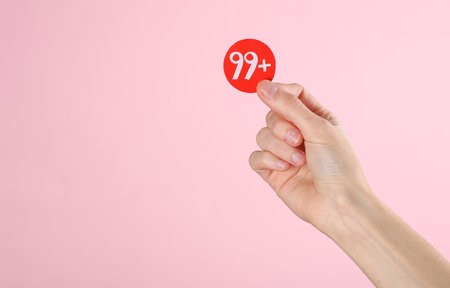 Hand holding paper cut notification with number 99 on pink background. Social media, message, sms,...