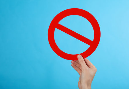 Hand holding red prohibition sign on a blue backgroundの写真素材