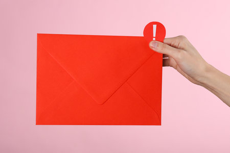 Hand holding red envelope with important notification on pink background. Social media chat, message, sms, subscribe notice alert and reminder.の写真素材