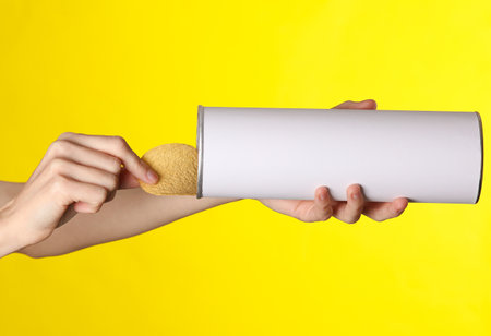 Woman's hand holds a cylindrical tin can for chips with a white empty label on yellow background. Template for designの写真素材