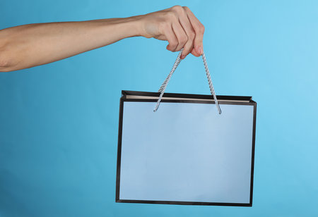 Woman's hand holds cardboard shopping bag on a blue background. sale, shopping conceptの写真素材