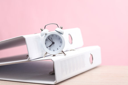 Office work, business concept. Alarm clock with folders on a pink backgroundの写真素材