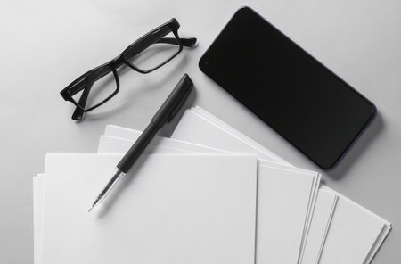 White blank sheets of a4 paper size or documents mockup and smartphone, eyeglasses and pen on a gray background. template for design. top view. flat layの写真素材