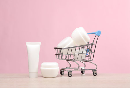 Mini Shopping cart with white cream tube and jars on pink background. beauty conceptの写真素材