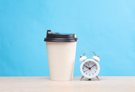 White coffee cup with alarm clock on table, blue backgroundの写真素材