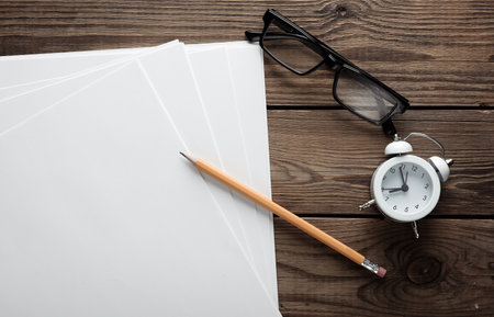 White blank sheets of a4 paper size or documents mockup with pencil, alarm clock and eyeglasses on wooden table. Template for designの写真素材