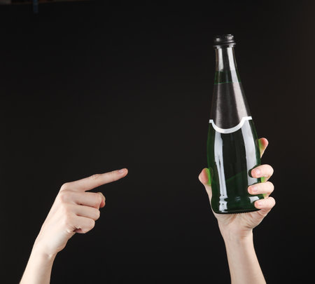 Female hand holding a bottle of green Irish beer on black backgroundの写真素材