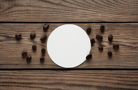 Mockup of white round coaster and coffee beans on wooden table. Template for designの写真素材