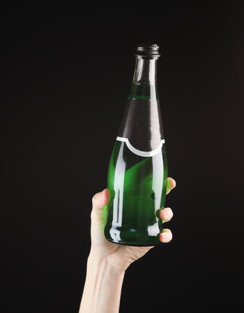 Female hand holding a bottle of green Irish beer on black backgroundの写真素材