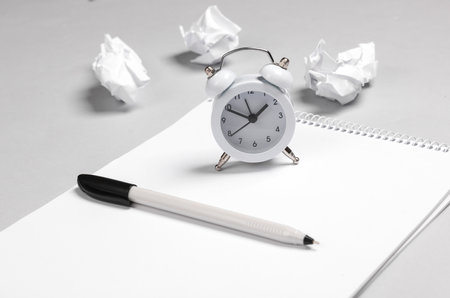 Lack of ideas. Sketchbook with crumpled paper, alarm clock and pen on gray background.の写真素材