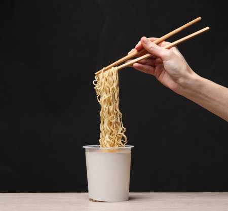 Woman's hand holding chinese chopsticks with instant noodles on black background. creative mockupの写真素材