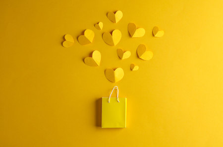 Miniature shopping bag with hearts on a yellow background. Sale, love, shopping concept. creative layoutの写真素材