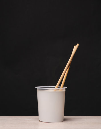 Cup with chinese chopsticks on a black background. instant noodles. template for design. creative mockupの写真素材