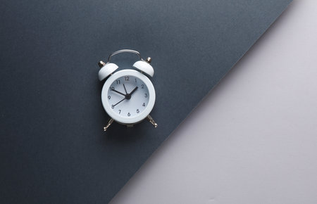 White alarm clock on black and gray background. creative layout. minimalist composition. top viewの写真素材