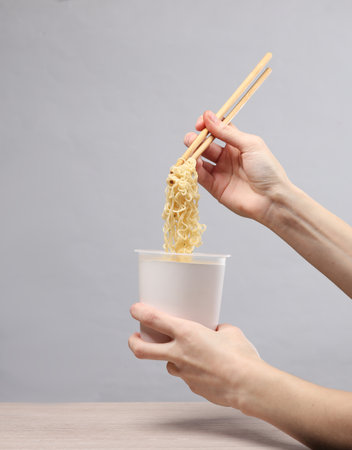 Woman's hand holding chinese chopsticks with instant noodles on gray background. creative mockupの写真素材