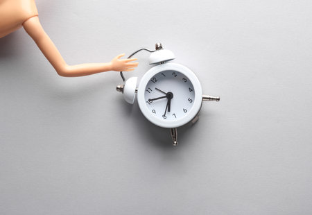 Doll's hand holding alarm clock on a gray background. creative minimal layout
