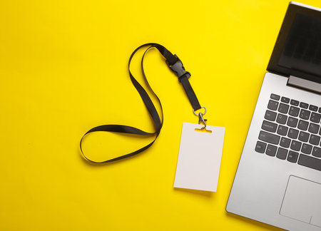 Laptop and Empty white ID card badge mockup on yellow background. Staff identity name tag. Space for text and design.の写真素材