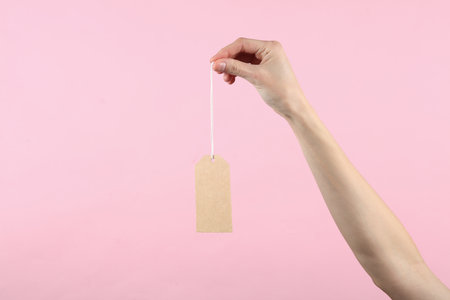 Craft empty price tag on a string in a female hand, pink background