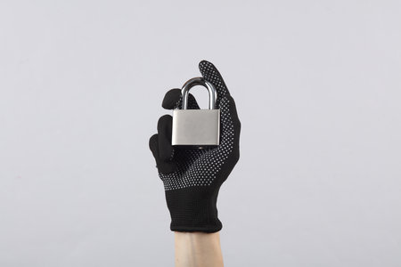 Female hand in working fabric glove holding lock on a gray backgroundの写真素材