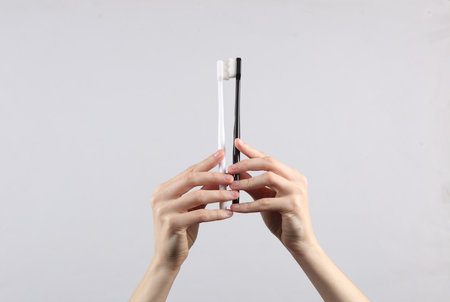 Female hands holding white and black toothbrushes on gray backgroundの写真素材