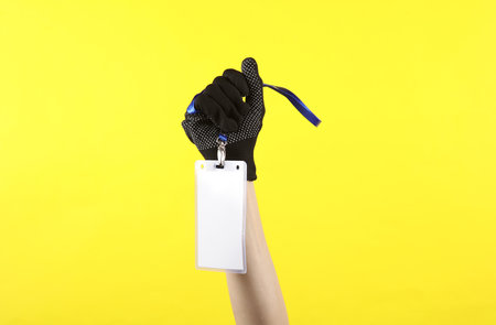 Female hand in working fabric glove holding Identification white blank id cards on yellow background