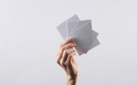 Hand holding White empty square memo sheets of paper on gray backgroundの写真素材