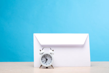 White envelope with alarm clock on the table, blue backgroundの写真素材