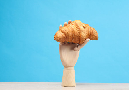 Wooden hand holding a croissant on a blue backgroundの写真素材