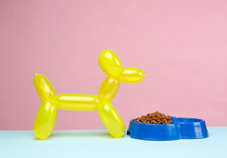 Balloon dog and bowl of dog food on a blue pink background.の写真素材