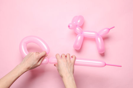 Female hands form a long balloon on a pink background with a balloon dog. Party, animators, birthday conceptの写真素材