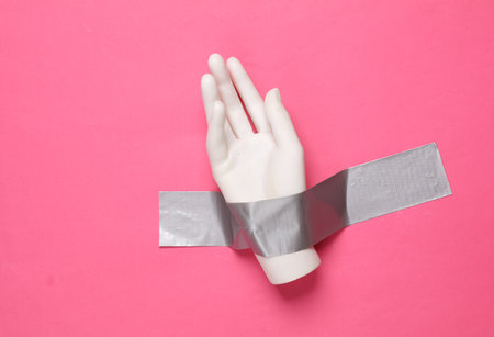 Plastic hand fixed with adhesive tape on a pink background. Conceptual pop, contemporary art, minimalist still lifeの写真素材