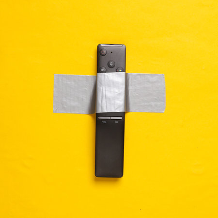 Tv remote fixed with adhesive tape on yellow background. Conceptual pop, contemporary art,...