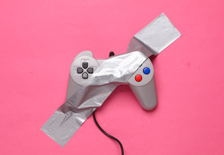 Retro gamepad fixed with adhesive tape on a pink background. Conceptual pop, video game