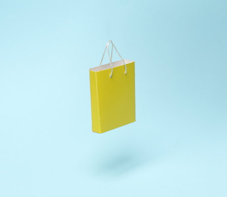 Miniature yellow shopping bag levitating on a blue background. shopping conceptの写真素材