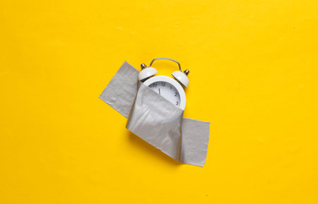 Alarm clock fixed with adhesive tape on yellow background. Conceptual pop, contemporary art, minimalist still lifeの写真素材