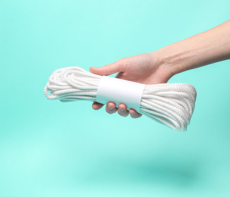 Woman's hand holds a coil of rope with a white empty tag on a blue backgroundの写真素材