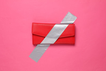 Red purse fixed with adhesive tape on a pink background. Conceptual pop, contemporary art, minimalist still lifeの写真素材