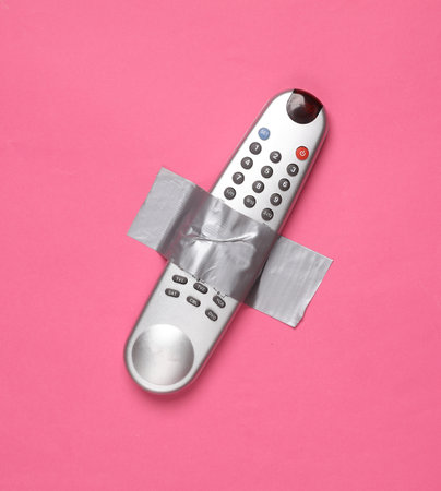 Tv remote fixed with adhesive tape on a pink background. Conceptual pop, contemporary art, minimalist still lifeの写真素材