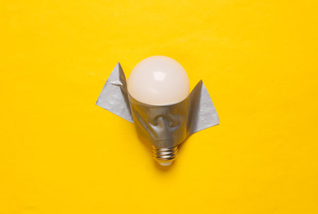 Light bulb fixed with adhesive tape on yellow background. Conceptual pop, contemporary artの写真素材