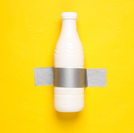 Milk bottle fixed with adhesive tape on yellow background. Conceptual pop, contemporary artの写真素材