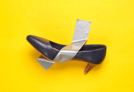 Women's heels shoes fixed with adhesive tape on yellow background. Conceptual pop, contemporary artの写真素材