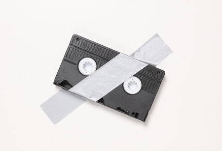Video cassette fixed with adhesive tape on white background. Conceptual pop, contemporary art, minimalist still lifeの写真素材