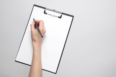 Female hand write on a blank sheet in clipboard on a gray background. Mockup, template for designの写真素材