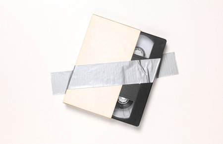 Video cassette fixed with adhesive tape on white background. Conceptual pop, contemporary art, minimalist still lifeの写真素材