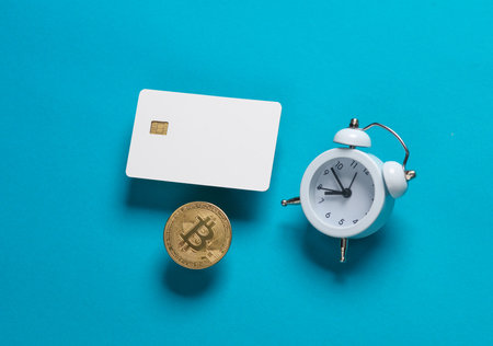 Mockup of white blank bank card with chip, bitcoin and alarm clock on blue background. template for...