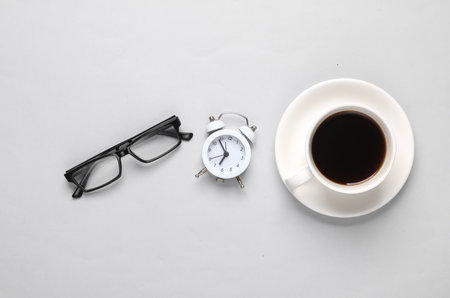 coffee cup with alarm clock and eyeglasses on a gray background. business conceptの写真素材