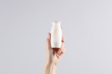 Female hand holding a bottle of yogurt on a gray backgroundの写真素材