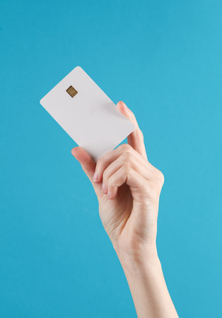 Woman's hand holds a white empty bank card with a chip on blue background. Layout, mockup, template...