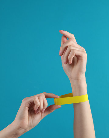 Female hand with a yellow paper bracelet on a blue background