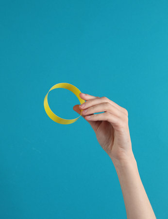 Female hand holding yellow paper bracelet on a blue background
